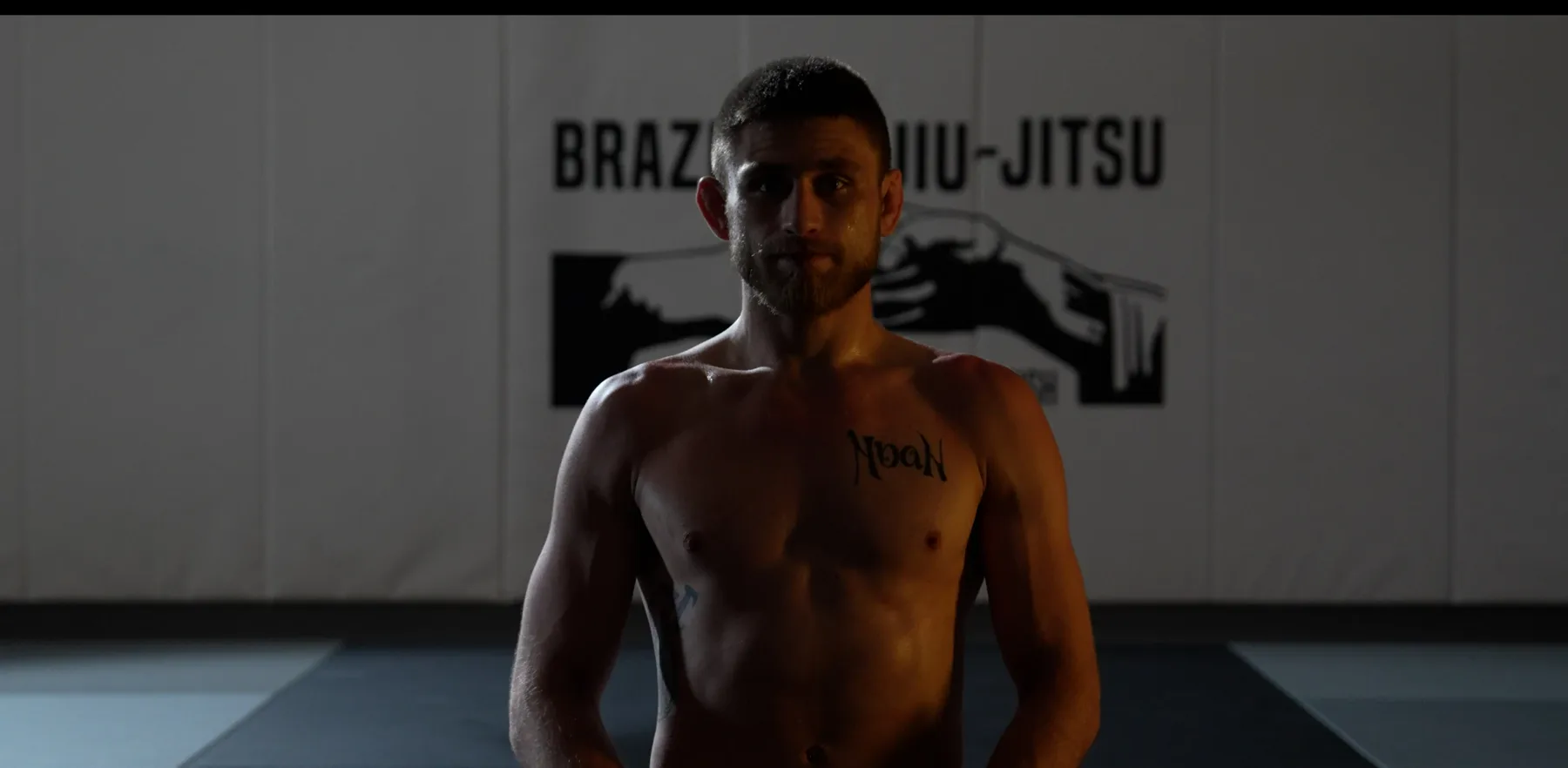 Backlit fighter standing in front of the Brazilian Jiu-Jitsu banner at Glacier Grappling & MMA in Columbia Falls, Montana