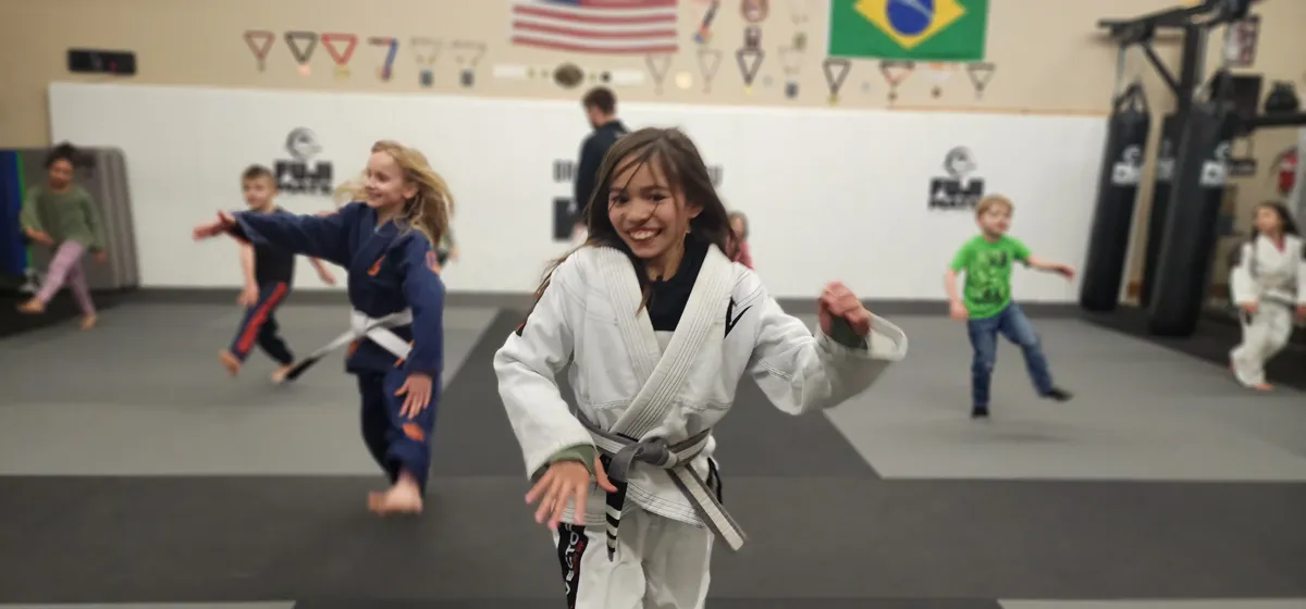 A smiling young student in a white gi during a kids Brazilian Jiu-Jitsu class